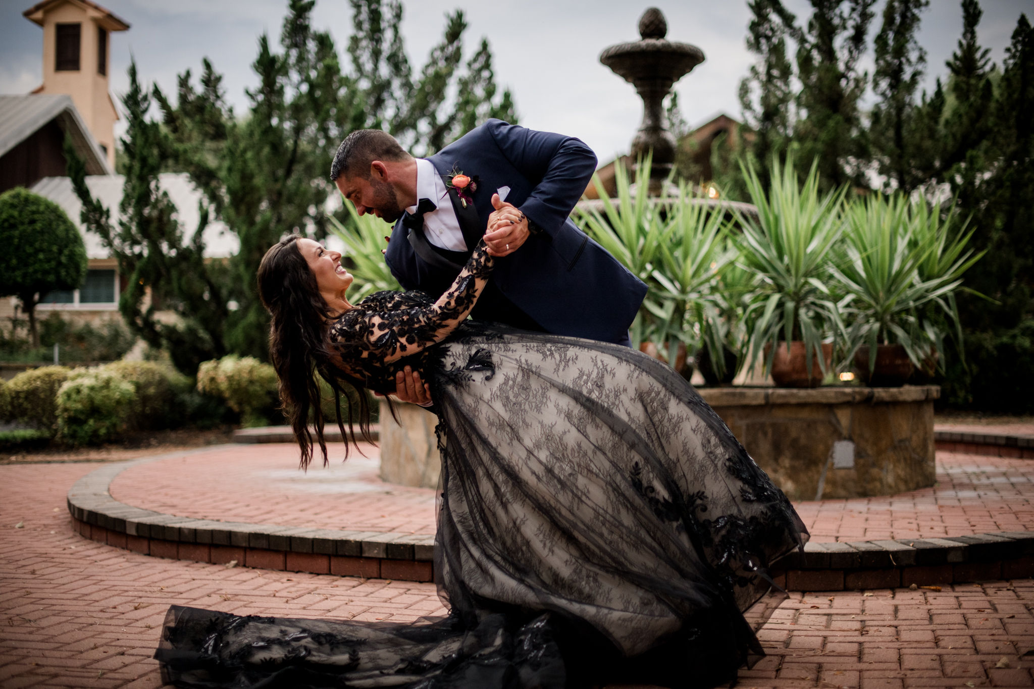Groom dipping Bride in a black wedding dress standing in front of a massive fountain with Palms surrounding it at a Houston wedding venue by Jamie Hardin, photographer