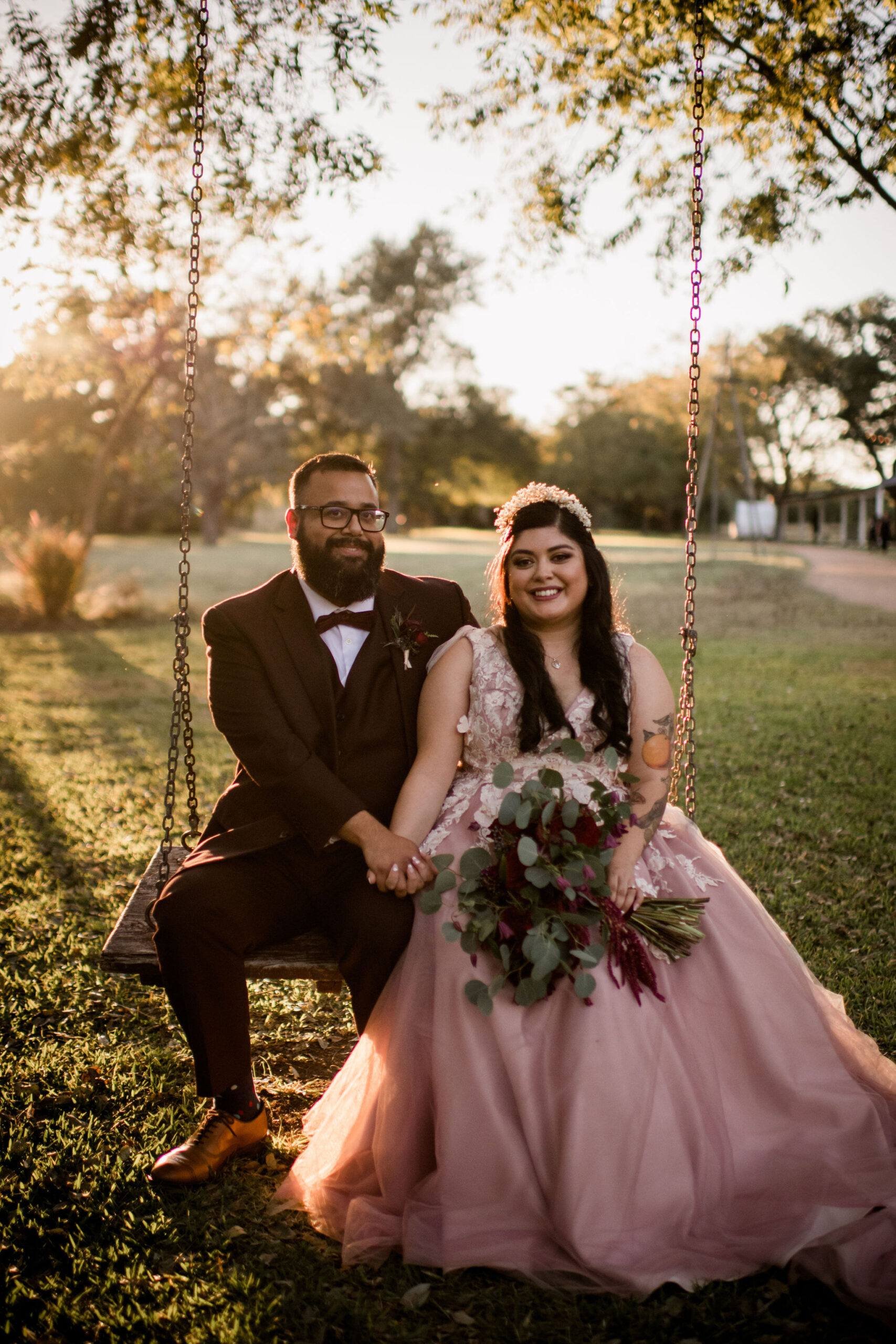 Bride and Groom holding hands sitting on a swing with the setting sun pouring in behind them as they smile at the camera, photo by Houston Wedding Photographer Jamie Hardin Photography