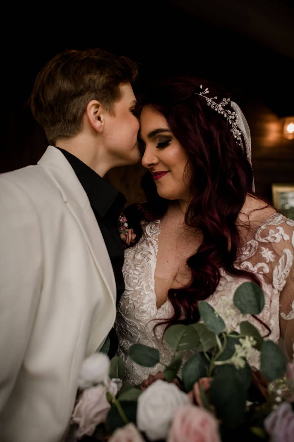 the texas bride in a white tuxedo is kissing her bride in a white wedding dress under the porch of Peach Creek Ranch