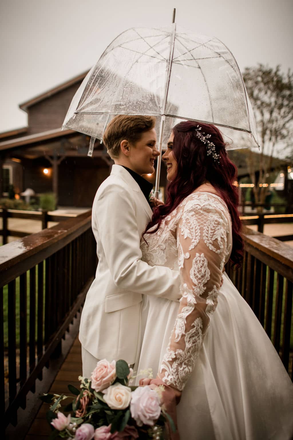 a close up of the texas brides posed at the front of the walk way of Peach Creek Ranch kissing under an umbrella in the texas rain