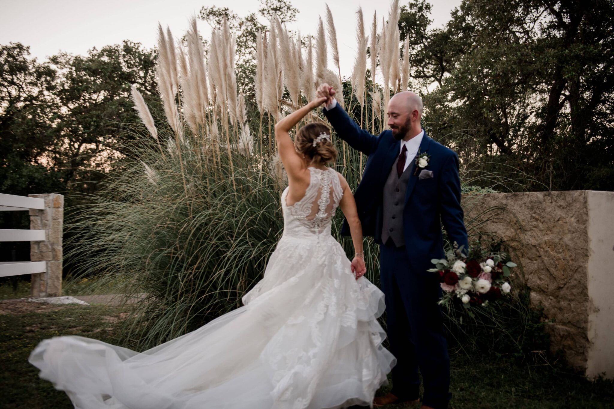 the texas bride and groom are in the courtyard of the inn at quarry ridge in their wedding attire dancing in front of cat tails