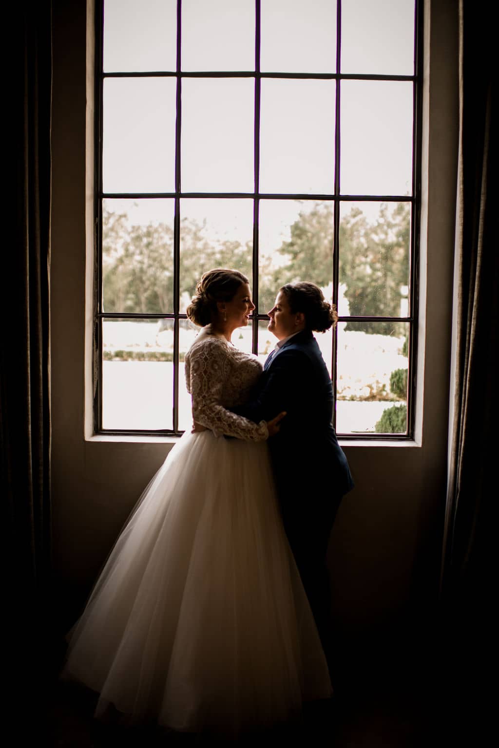 two brides silhouetted in front of the window at a bryan-college station wedding venue in an silhouette