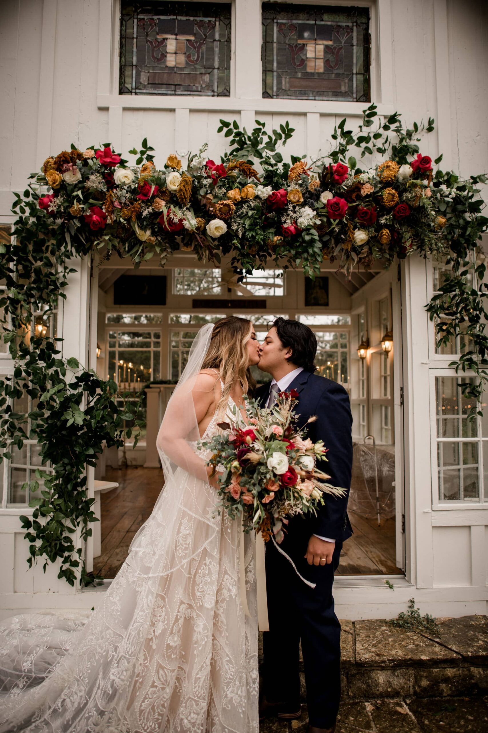 bride and groom kiss under the flower arch from their wedding ceremony