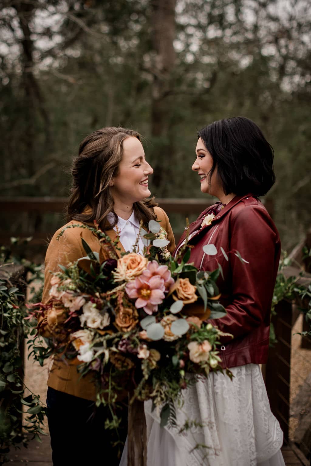 the two brides are laughing while holding a floral bouquet designed by texas wedding florist urban rubbish