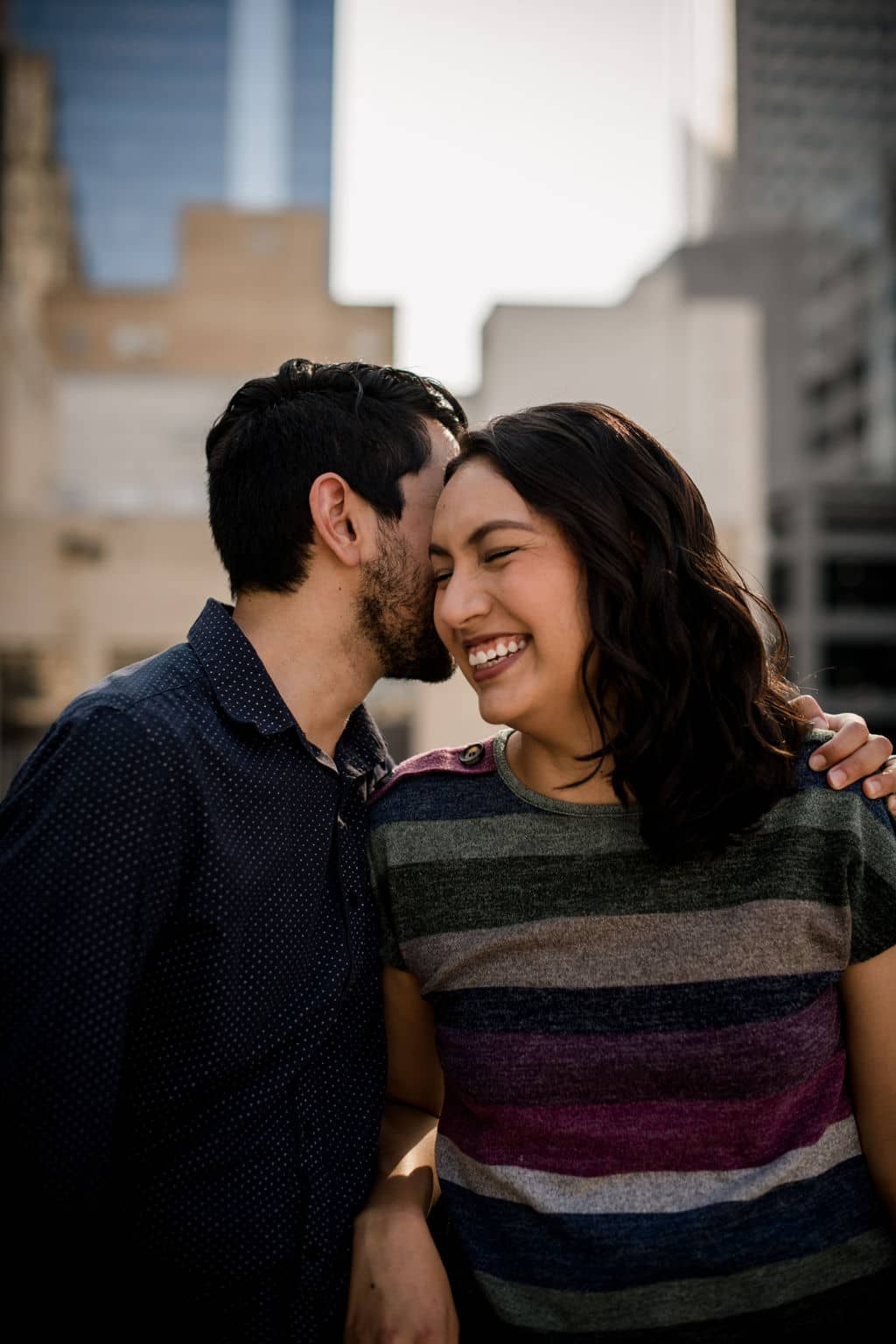the couple is laughing and smiling in their engagement photo outfits on a texas rooftop