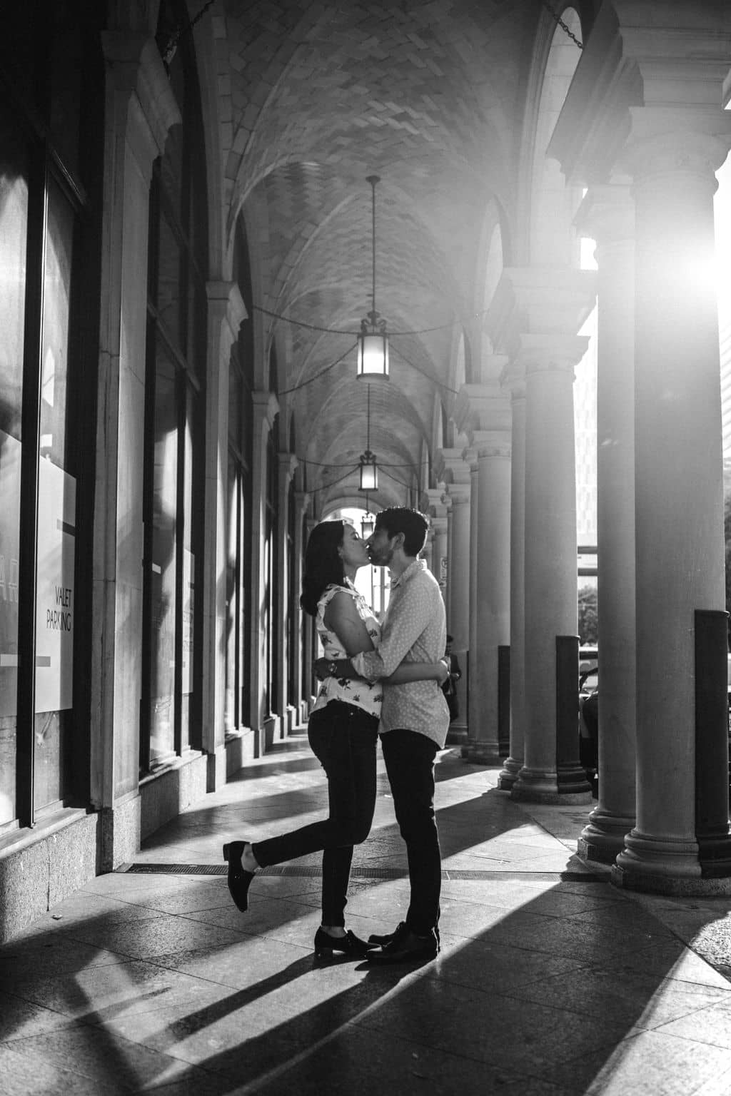 the future bride and groom are kissing holding each other in a hall of pillars