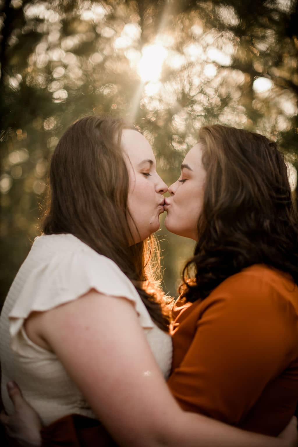 the future brides are embracing each other and kissing in their engagement photo outfits