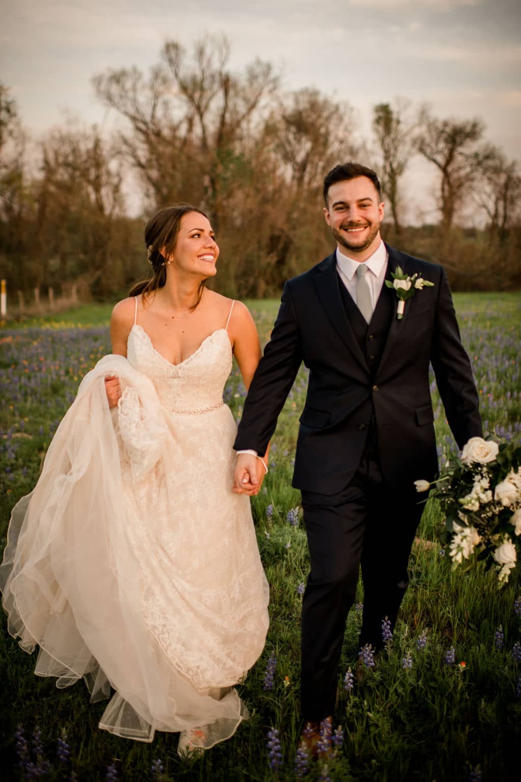 the bride and groom are walking towards the camera in a local field of wild flowers in the bryan college station texas area