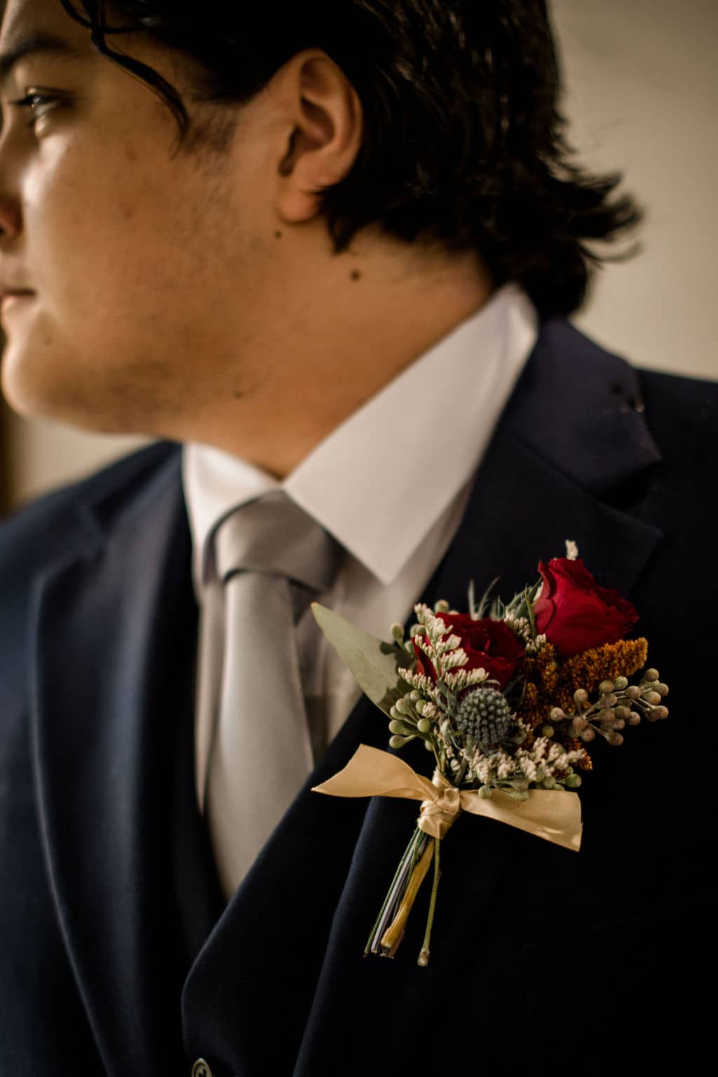 the groom is facing away from the camera while focusing on his floral boutonniere designed by texas wedding florist Urban Rubbish