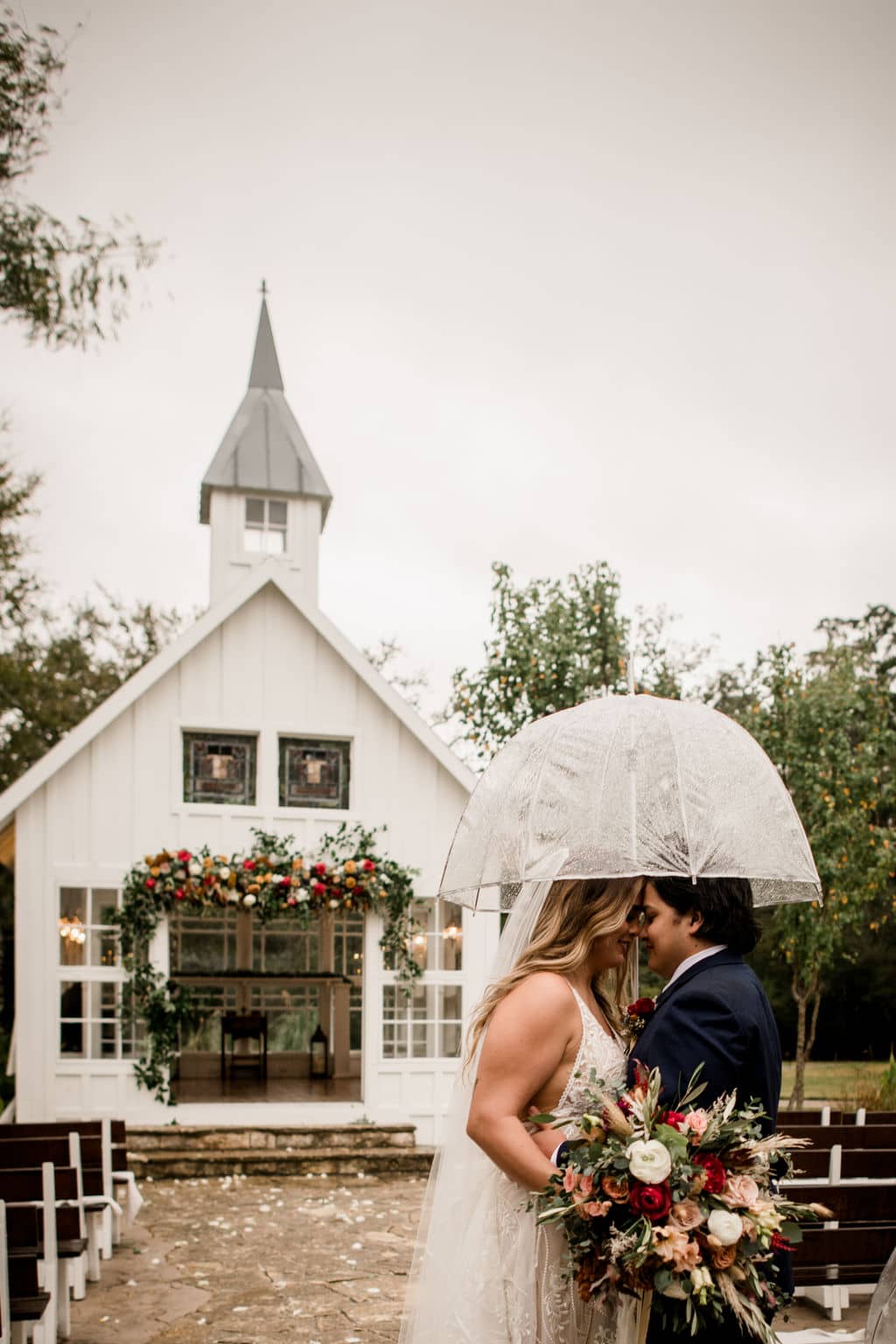 the bride and groom are kissing in the rain while holding up the bridal bouquet designed by urban rubbish