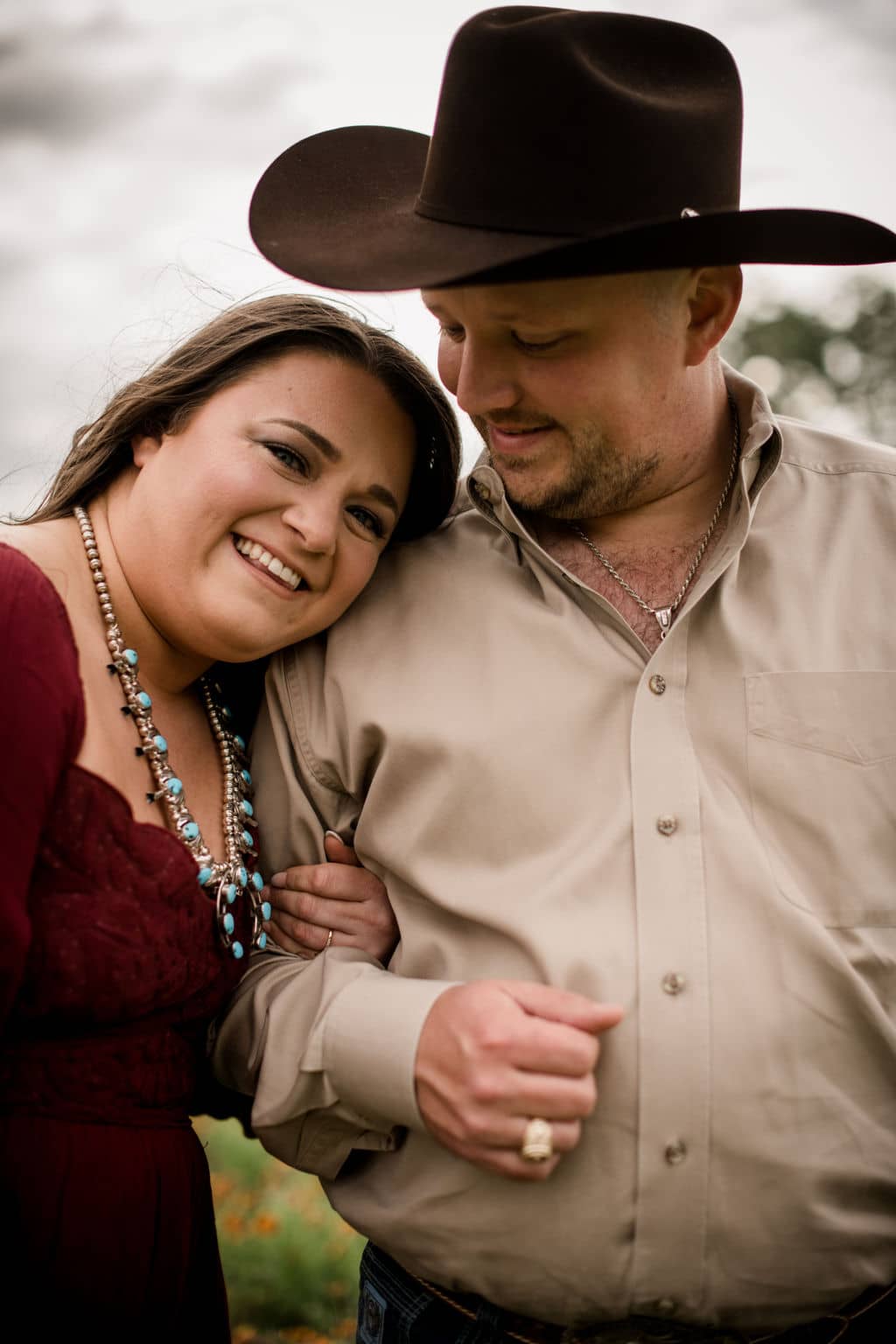 the future bride and groom are dressed in classic texas attire for their engagement photo outfits with a statement necklace