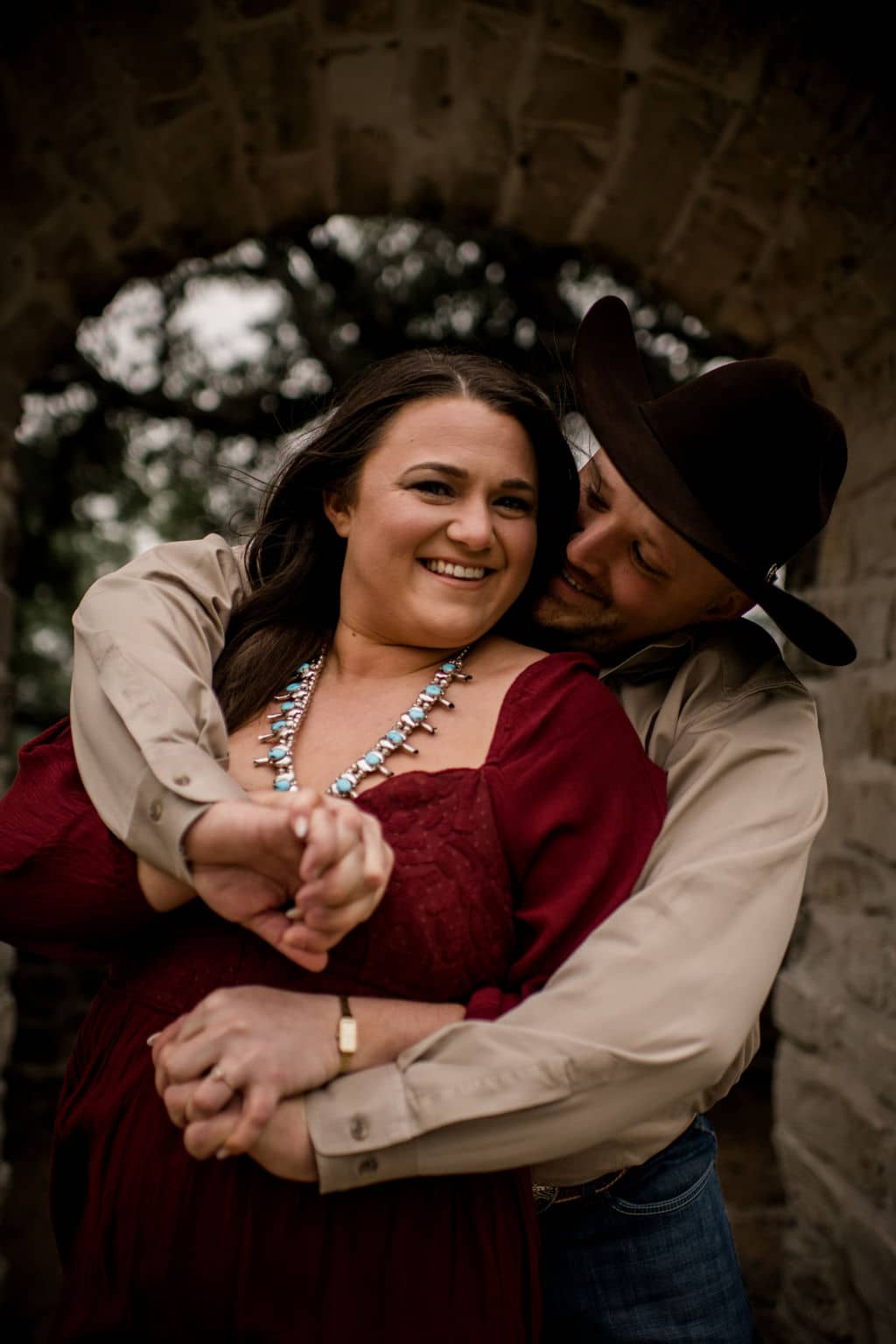 the future groom is holding his future bride from behind while she wears a statement necklace