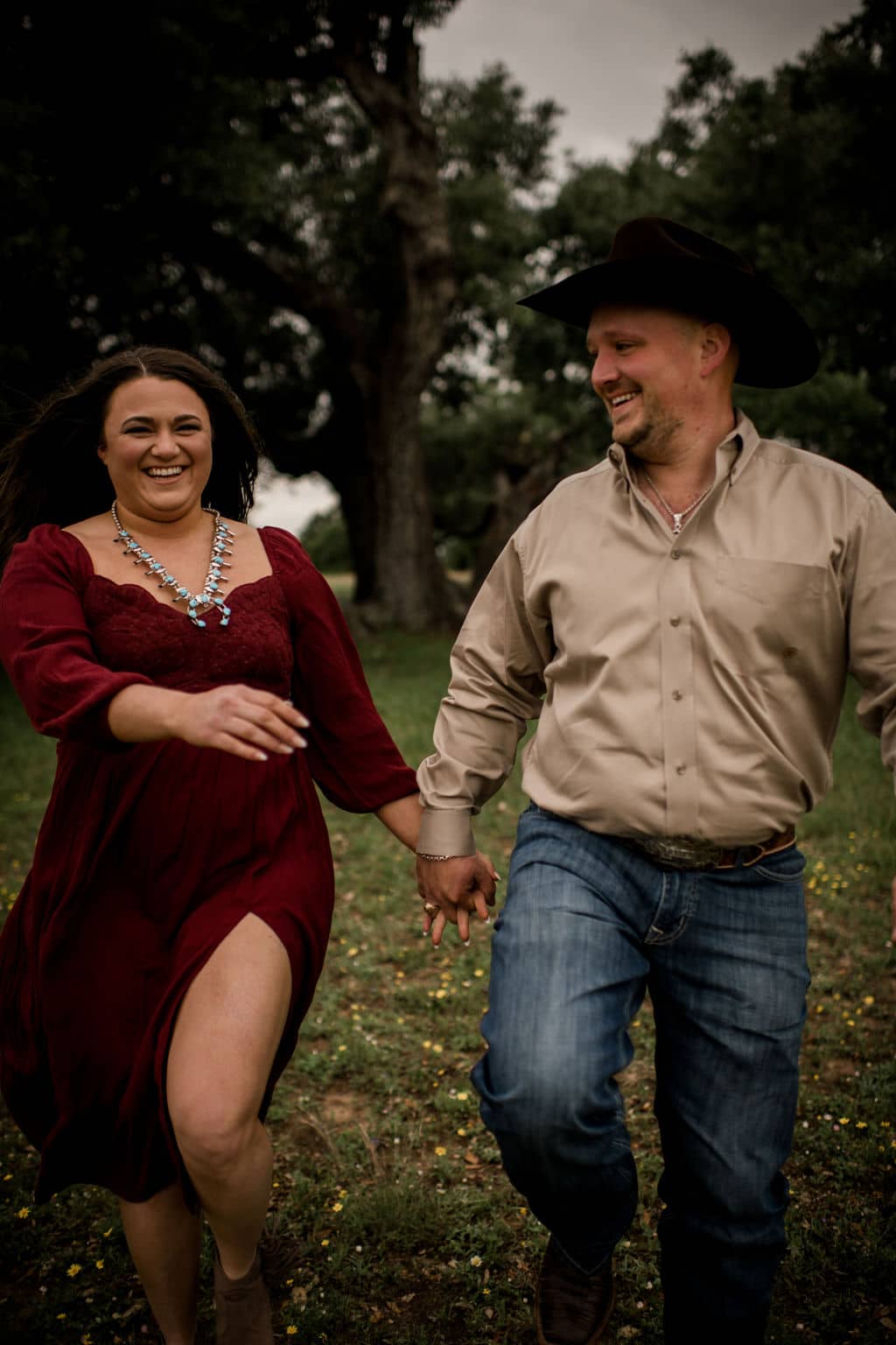the future texas bride and groom are holding hands walking down a field in their engagement photo outfits