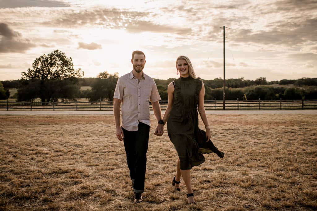the future bride and groom are walking down a field in texas in their engagement photo outfits