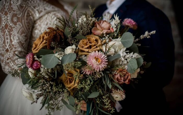 the texas bride and groom are standing behind an intricate bouquet done by urban rubbish