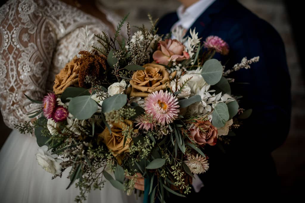 the texas bride and groom are standing behind an intricate bouquet done by urban rubbish