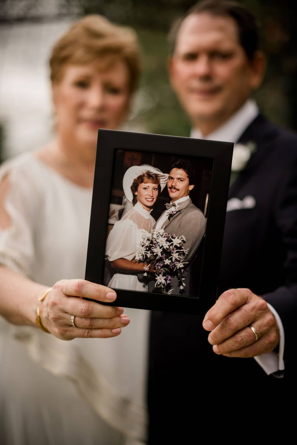 the husband and wife pose holding up a photo from their wedding day on their vow renewal.