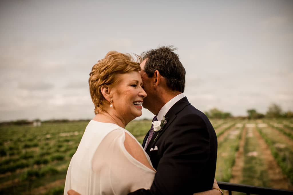 the husband and wife embrace each other overlooking a texas vineyard after their vow renewal
