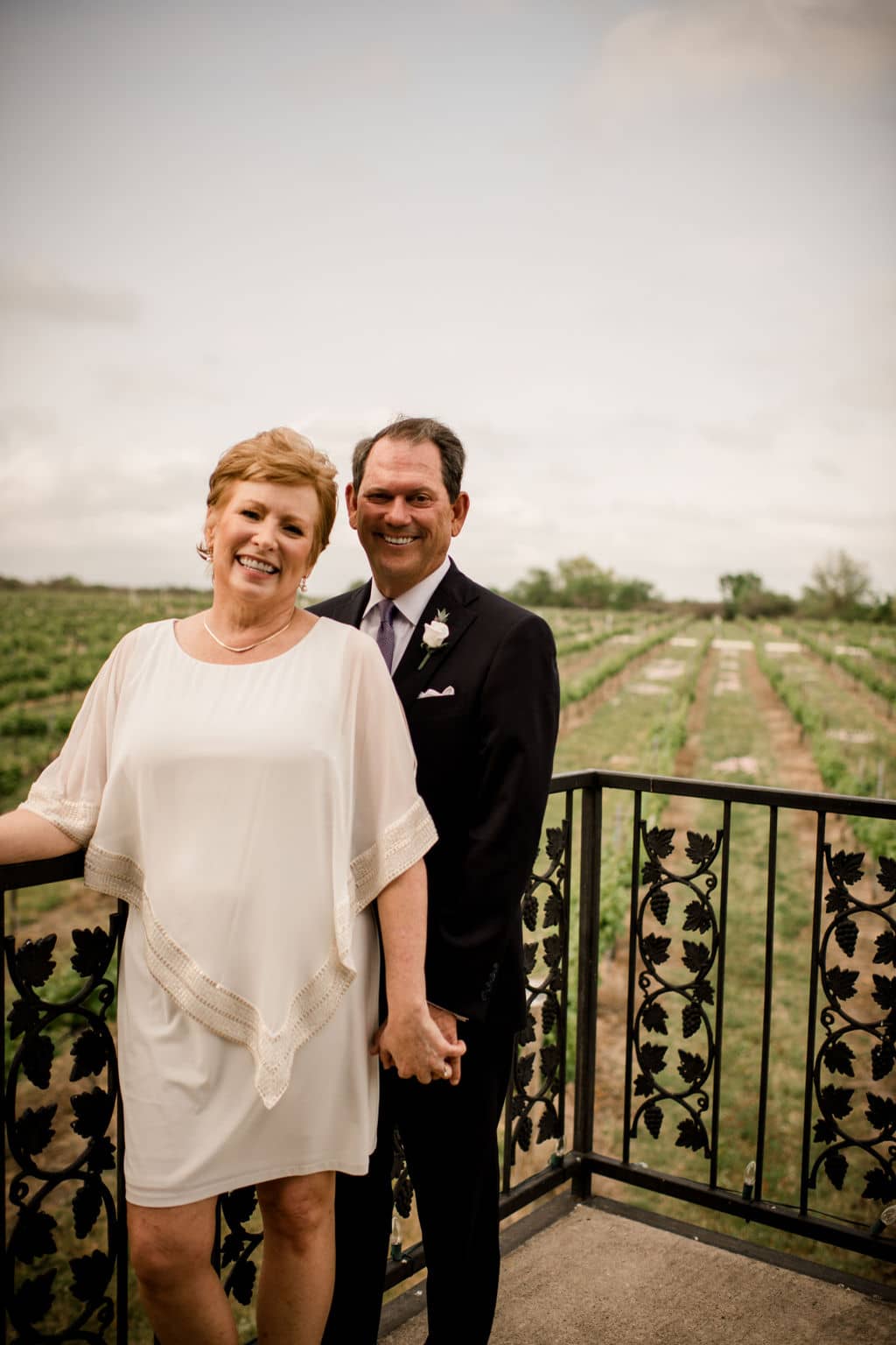 husband and wife pose in their vow renewal attire in front of a Texas vineyard